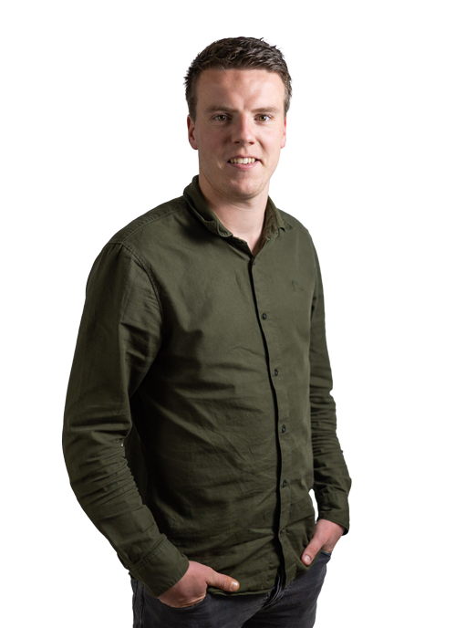 Portret van Teun Van den Boom. Hij draagt een donkergroen hemd met lange mouwen en een donkere jeansbroek. Hij heeft beide handen in zijn zakken en lacht naar de camera. 